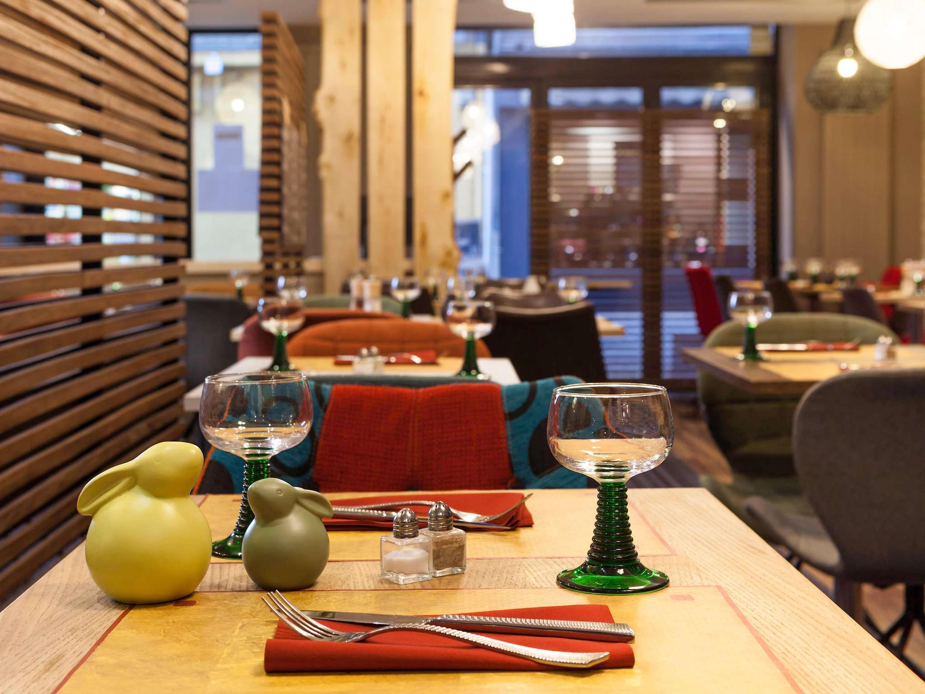 A restaurant interior with tables set for dining, featuring wooden slats on the walls and a view of the cityscape through large windows.