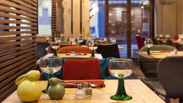 A restaurant interior with tables set for dining, featuring wooden slats on the walls and a view of the cityscape through large windows.