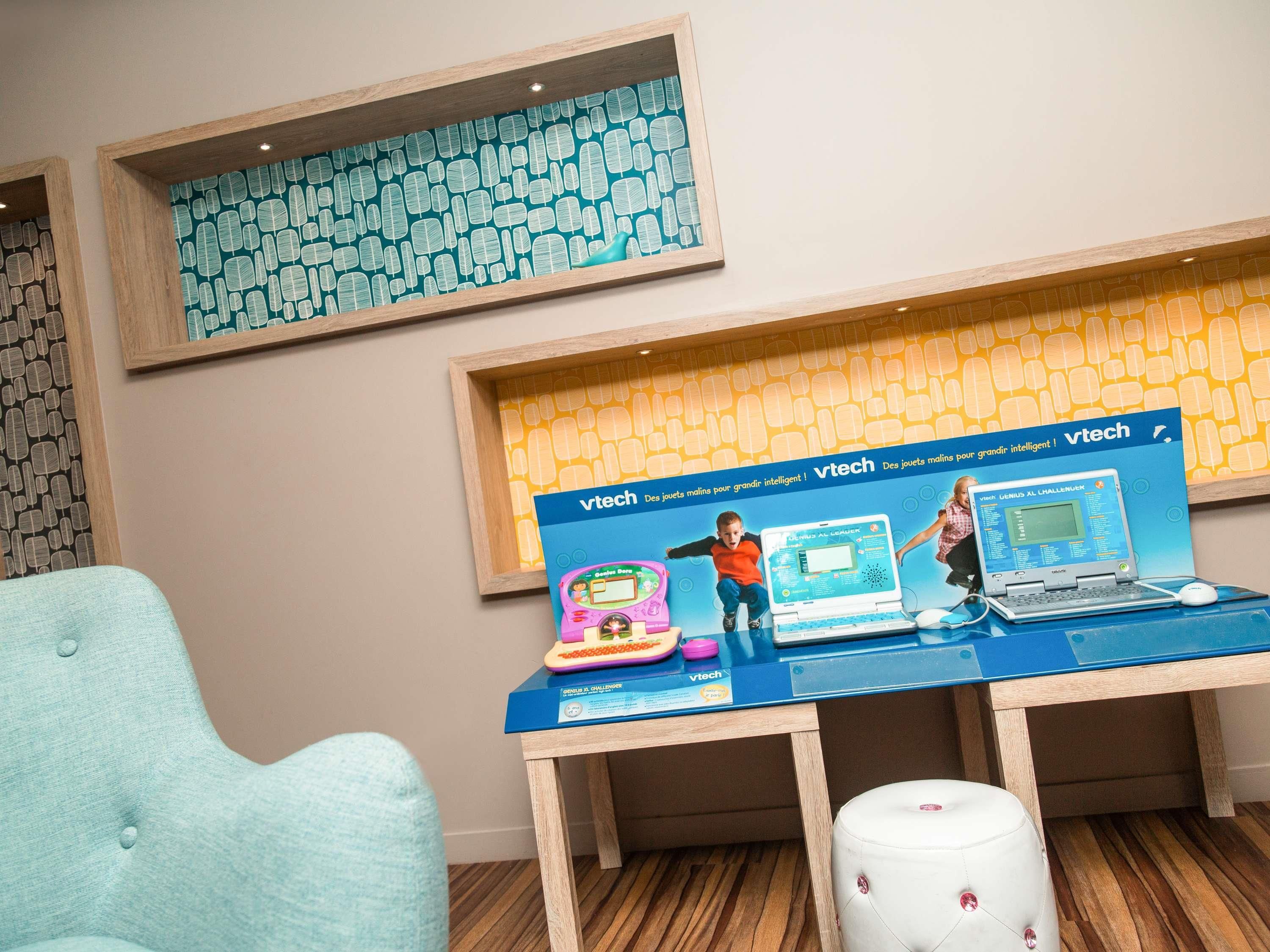 A room with a blue table displaying educational toys and a laptop, a light blue chair, and a patterned wall.