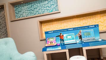 A room with a blue table displaying educational toys and a laptop, a light blue chair, and a patterned wall.