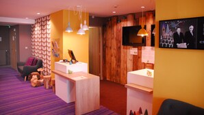 A lobby with a reception desk, wooden panel walls, a television, and a seating area with a purple carpet.