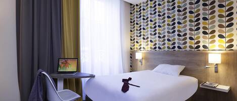 Habitación de hotel con cama, escritorio, computadora portátil, una silla y pared con diseño de hojas.
