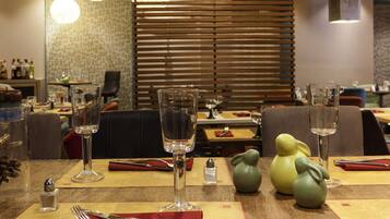 Un comedor con mesas dispuestas para dos, con cubertería, copas y jarrones decorativos.