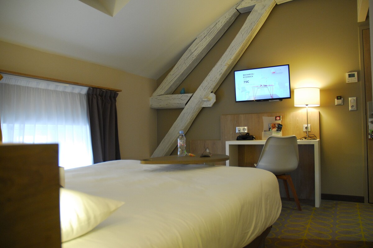 A hotel room with a bed, a desk, a chair, a television, and a lamp.