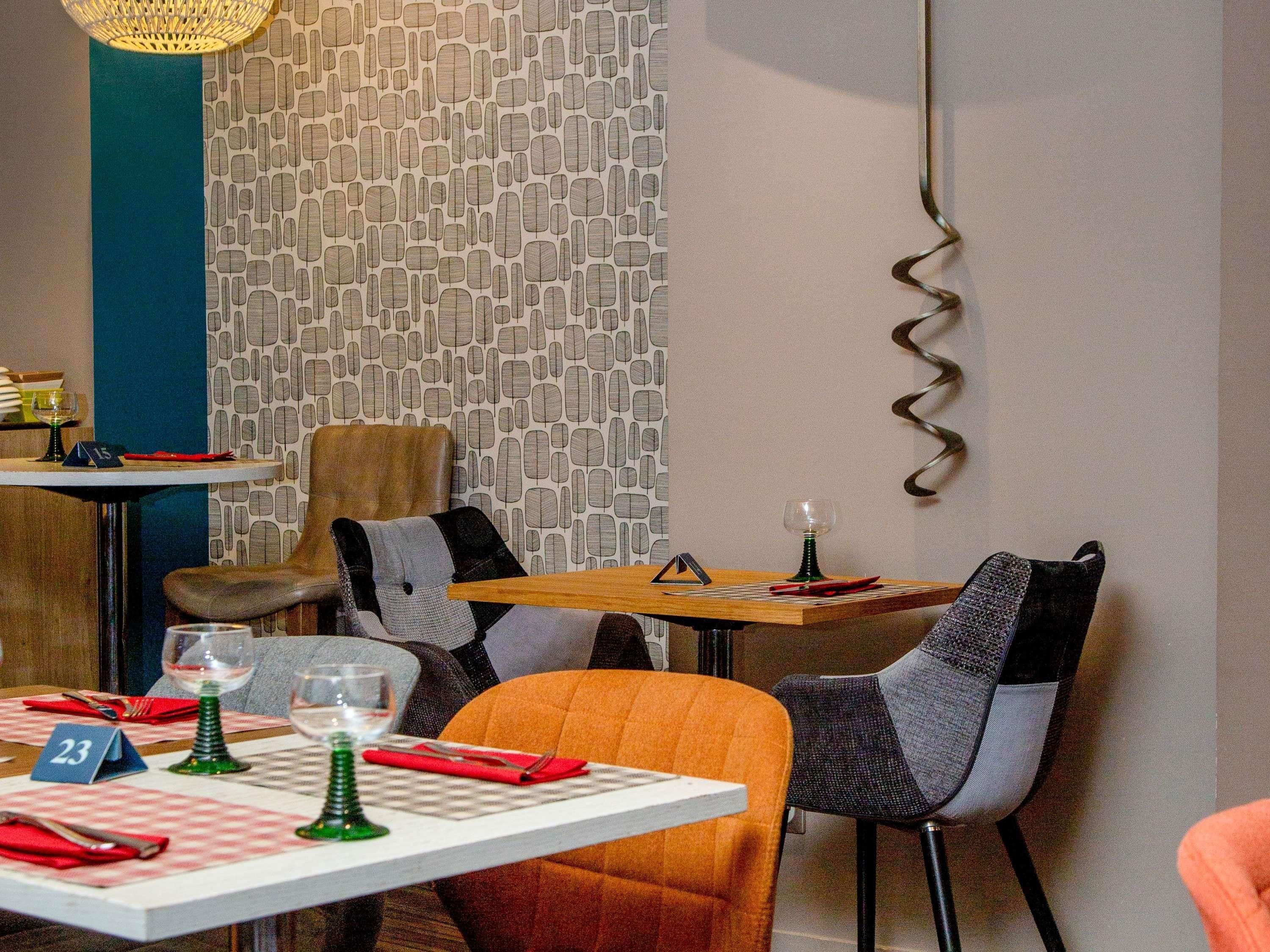 A dining area with tables set for two, chairs, and a patterned wall in the background.