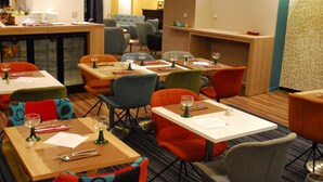 A restaurant with multiple tables and chairs, overhead lighting, and a bar area.