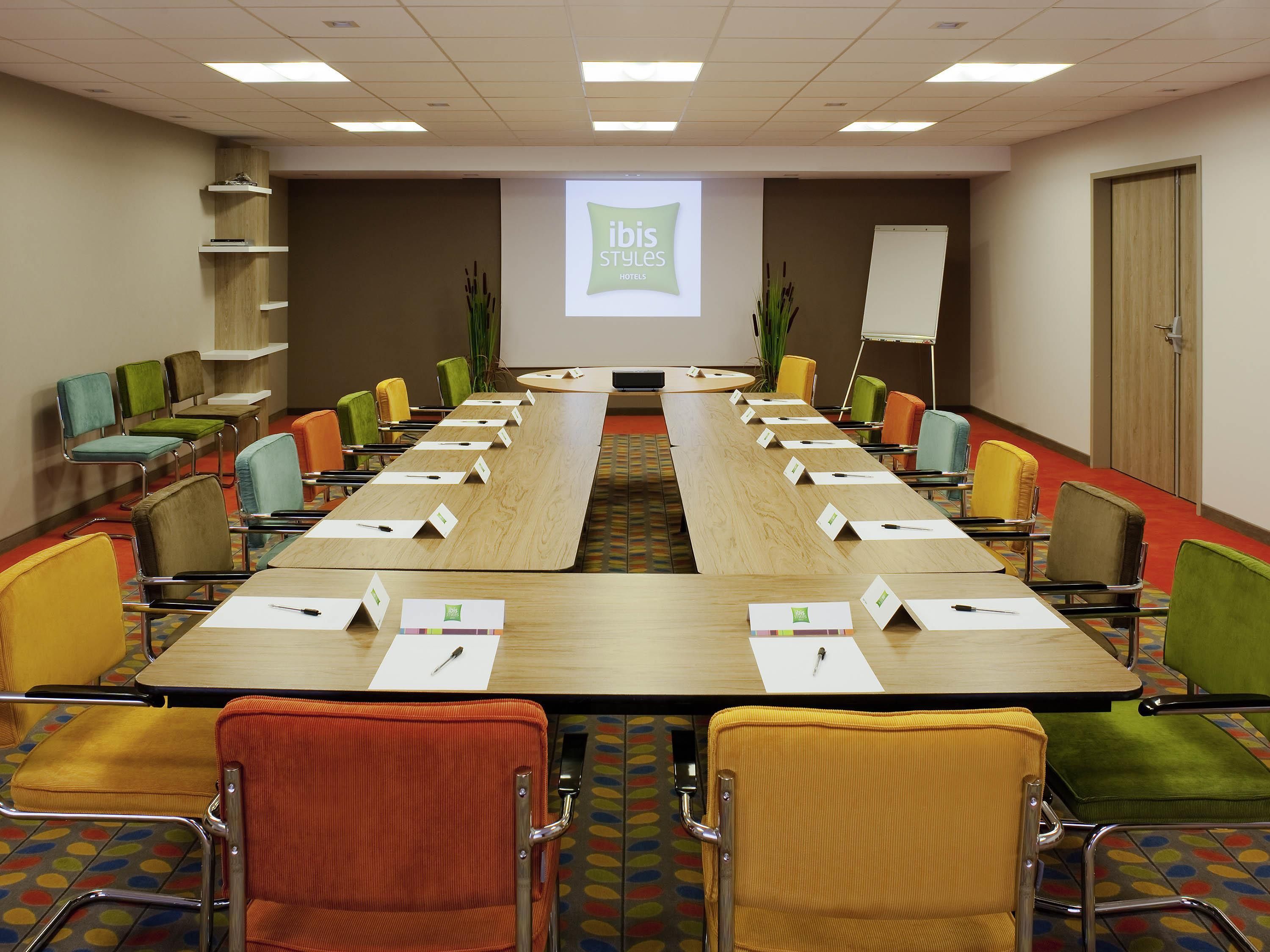 A conference room with a long table, multiple chairs, name cards, and a presentation screen.