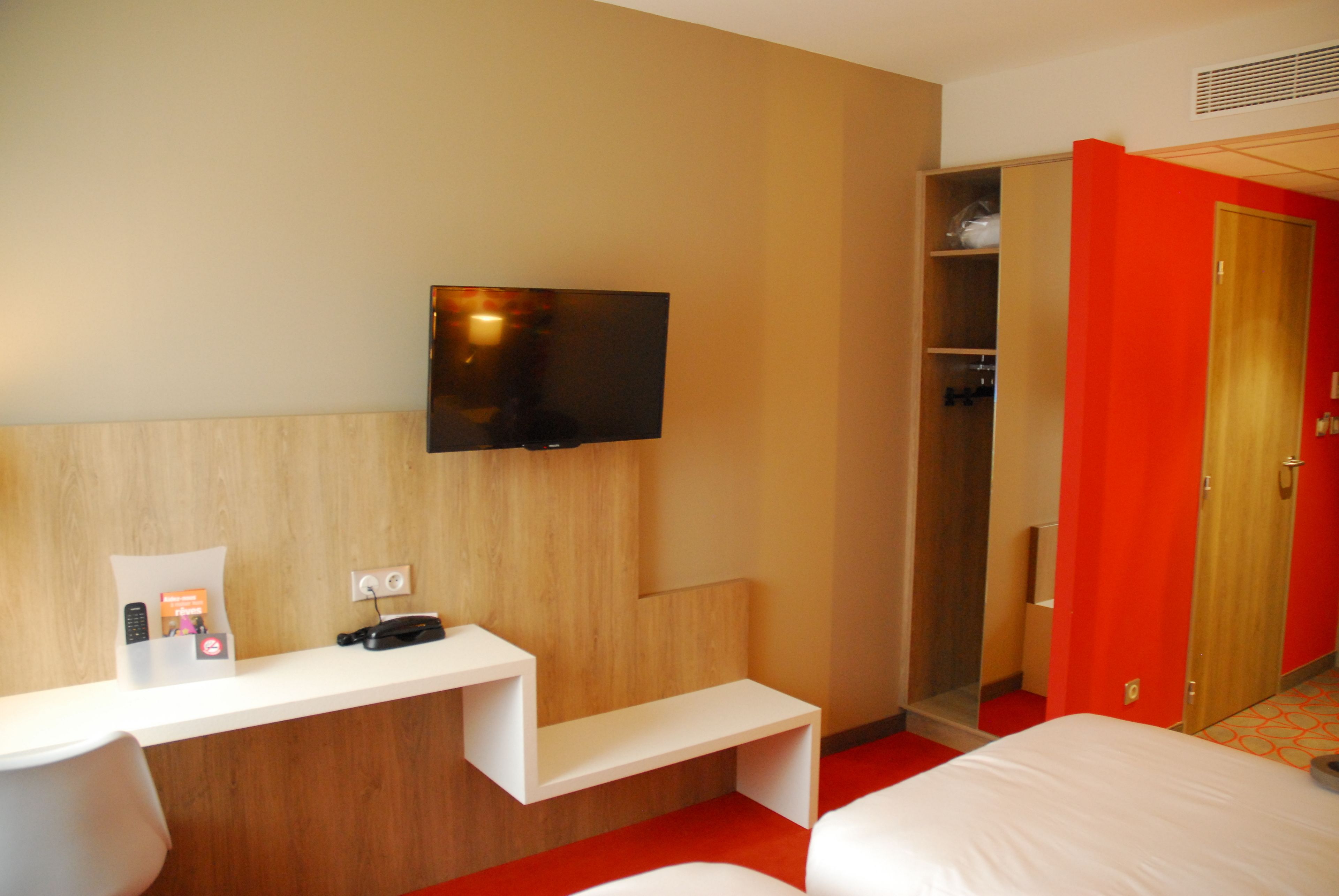 Ett hotellrum med en säng, ett skrivbord med en platt-TV, en spegel och en garderob.