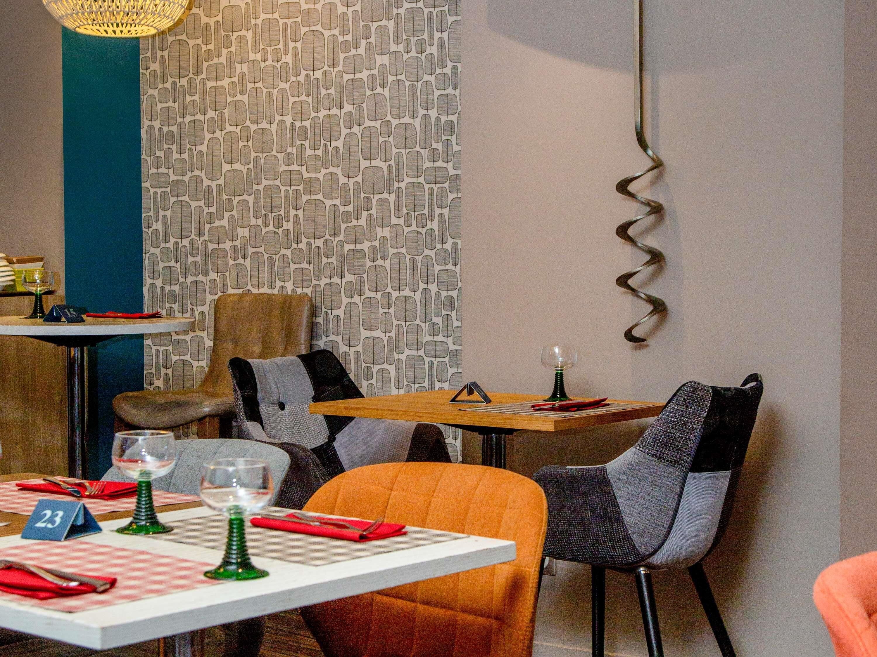 Un comedor con mesas dispuestas para dos personas, sillas y un papel tapiz decorativo.