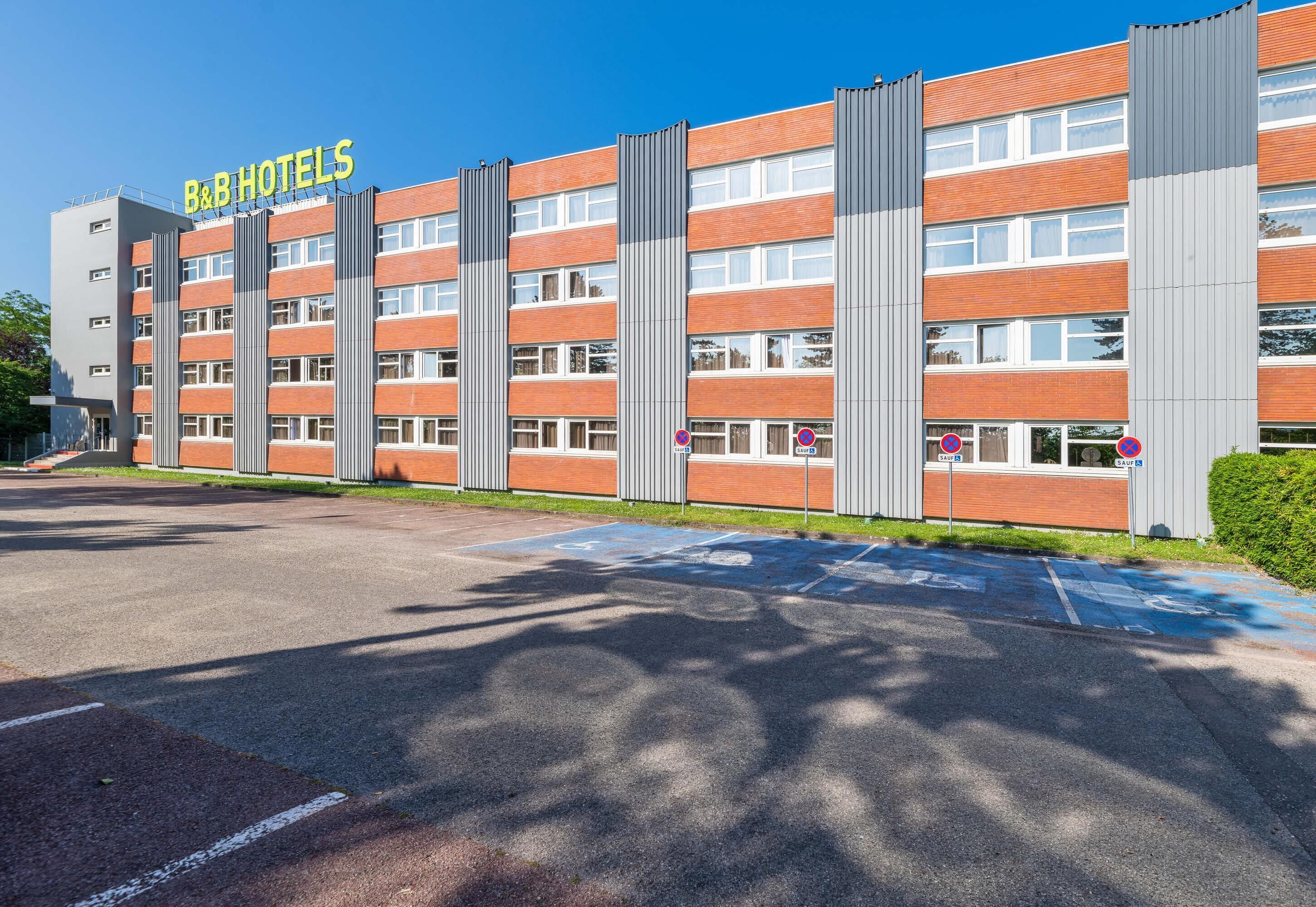 Un hotel tipo casa de huéspedes con fachada de ladrillo moderno, varias ventanas y un estacionamiento con espacios para discapacitados.