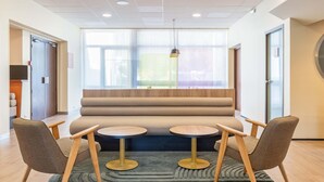 A modern waiting area with a sofa, two small round tables, and chairs. - B&B HOTEL Lyon Nord (Dardilly)