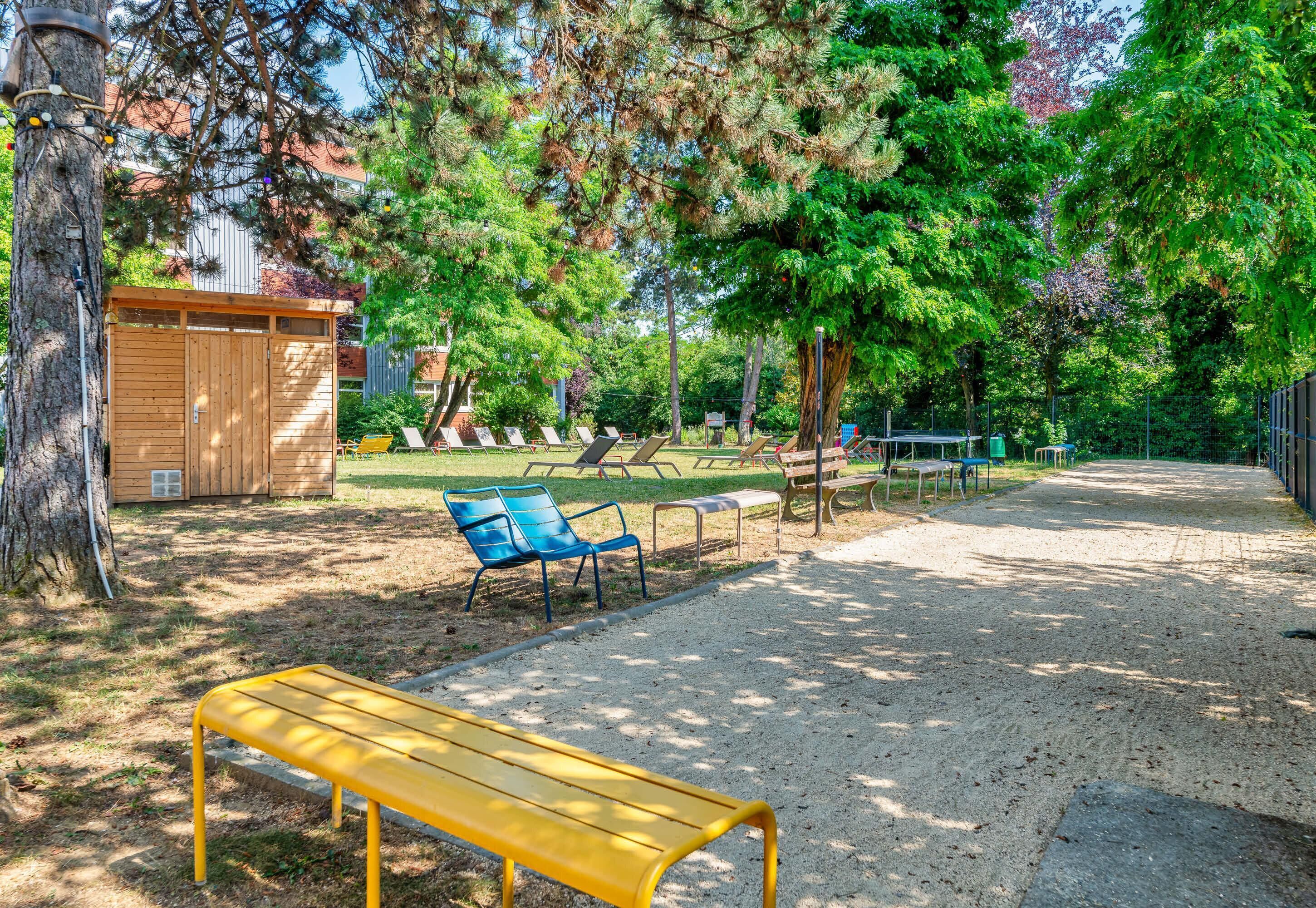 Un parc avec un banc jaune, des tables de pique-nique et des arbres.
