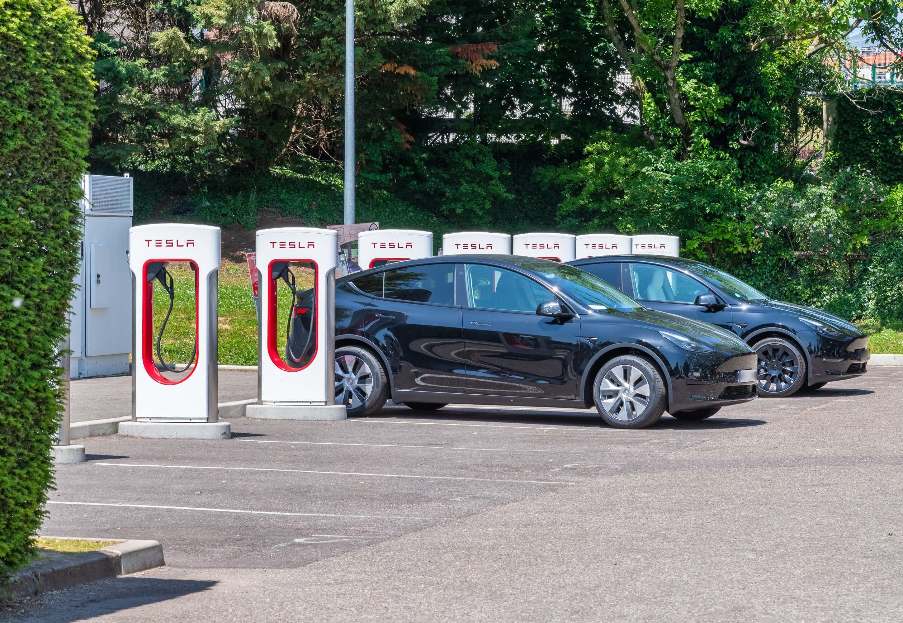 Une borne de recharge Tesla avec deux voitures garées à proximité.
