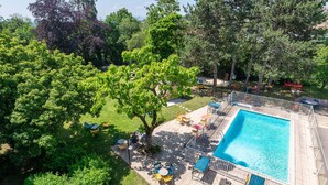 A swimming pool with a tiled deck, surrounded by trees and outdoor seating. - B&B HOTEL Lyon Nord (Dardilly)