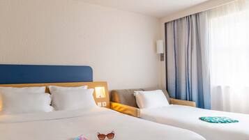 A hotel room with two beds, a headboard, a nightstand, a lamp, and a window with curtains.