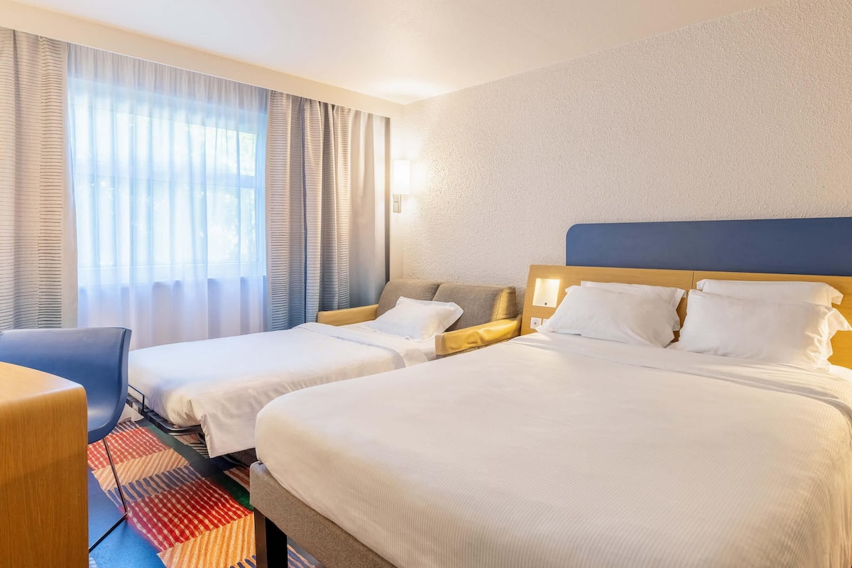 Ein Hotelzimmer mit zwei Betten, einem Schreibtisch und einem fenster mit Vorhängen.