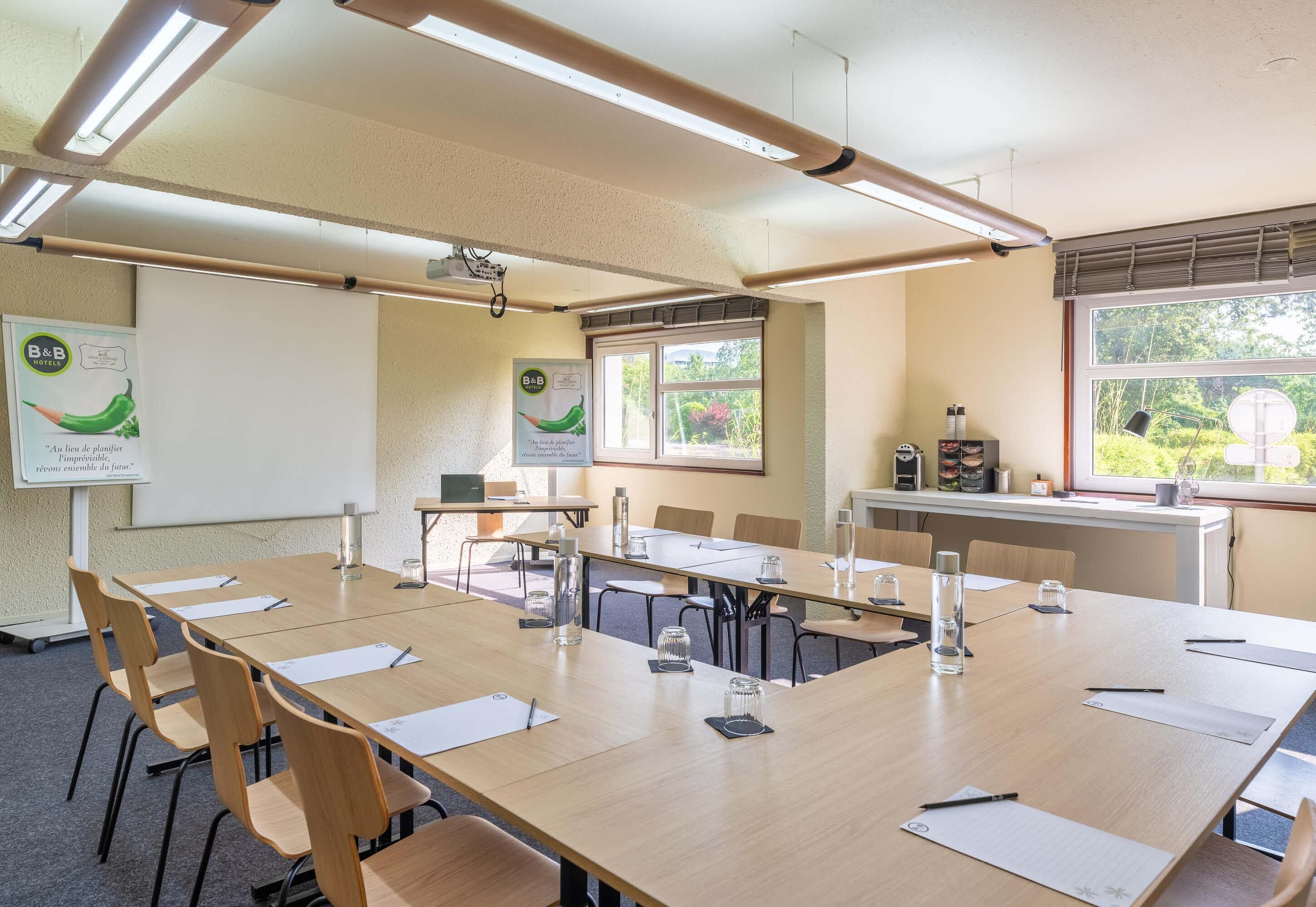 Une salle de conférence équipée d’une longue table, de chaises, d’un écran de projection et d’une fenêtre donnant sur un paysage verdoyant.