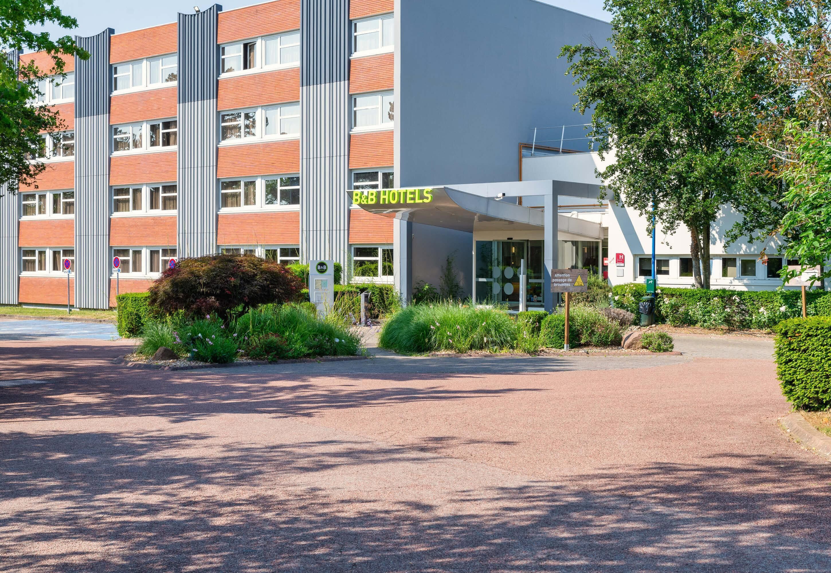 A hotel entrance with a modern building, a covered walkway, and a parking area.