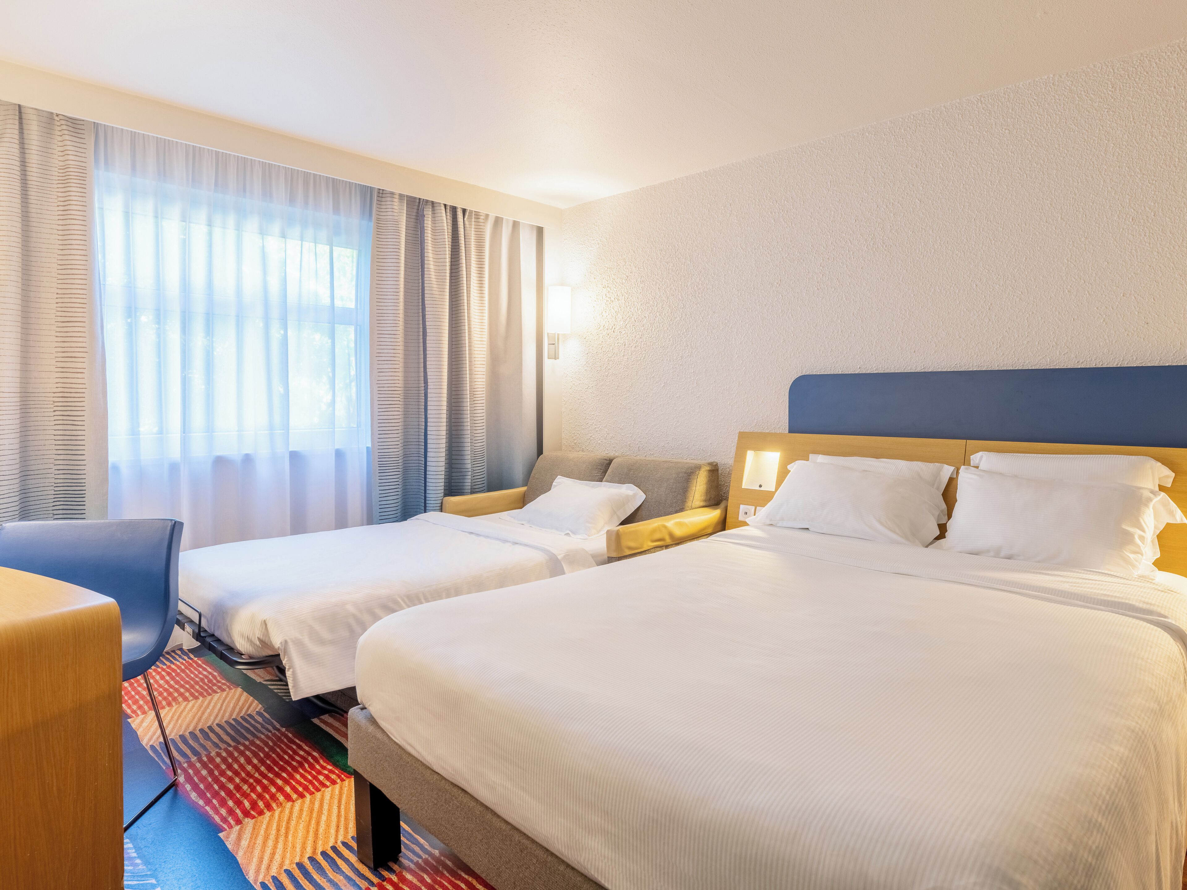 A hotel room with two beds, a desk, and a window with curtains.