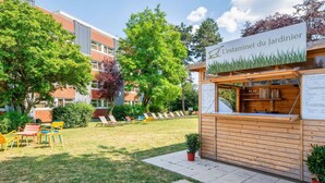 A garden café with a wooden structure, outdoor seating, and a sign reading "L'estaminet du Jardinier". - B&B HOTEL Lyon Nord (Dardilly)