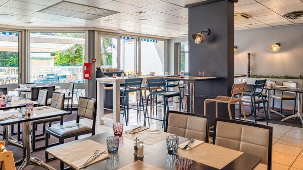A modern restaurant with multiple dining areas, large windows, and a mix of table and booth seating. - B&B HOTEL Lyon Nord (Dardilly)