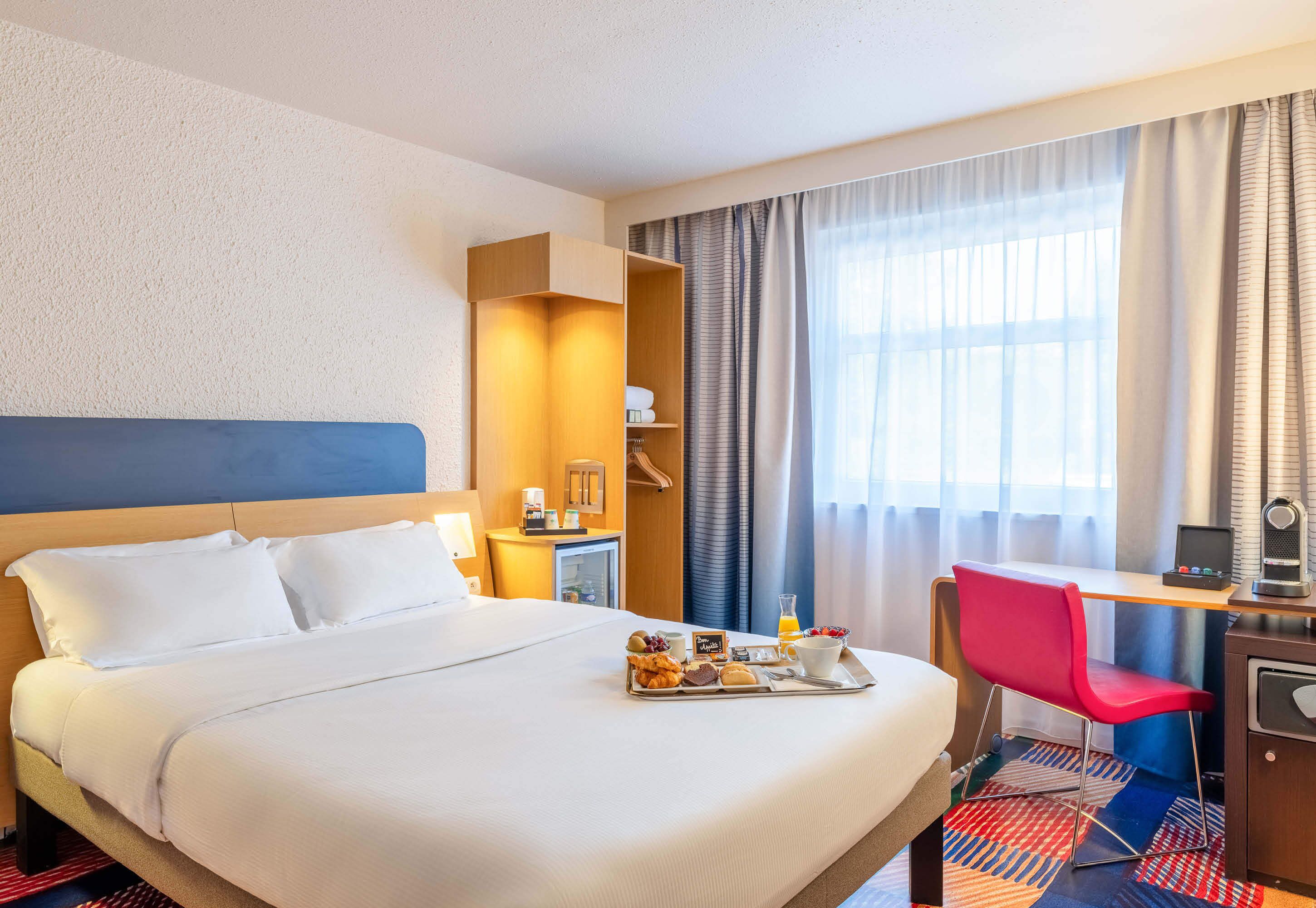 A hotel room with a bed, a desk, a chair, a tray with breakfast items, and a wardrobe.