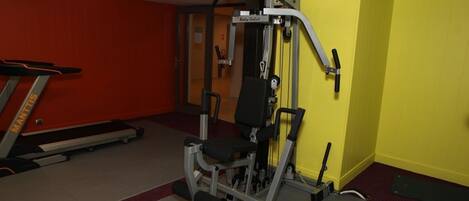 Une salle de sport équipée d’un tapis de course, d’une machine de musculation et d’un mur jaune.