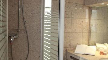 Une salle de bain moderne avec une douche à parois de verre, un mur recouvert de carreaux de marbre, un lavabo avec un miroir et une poubelle.