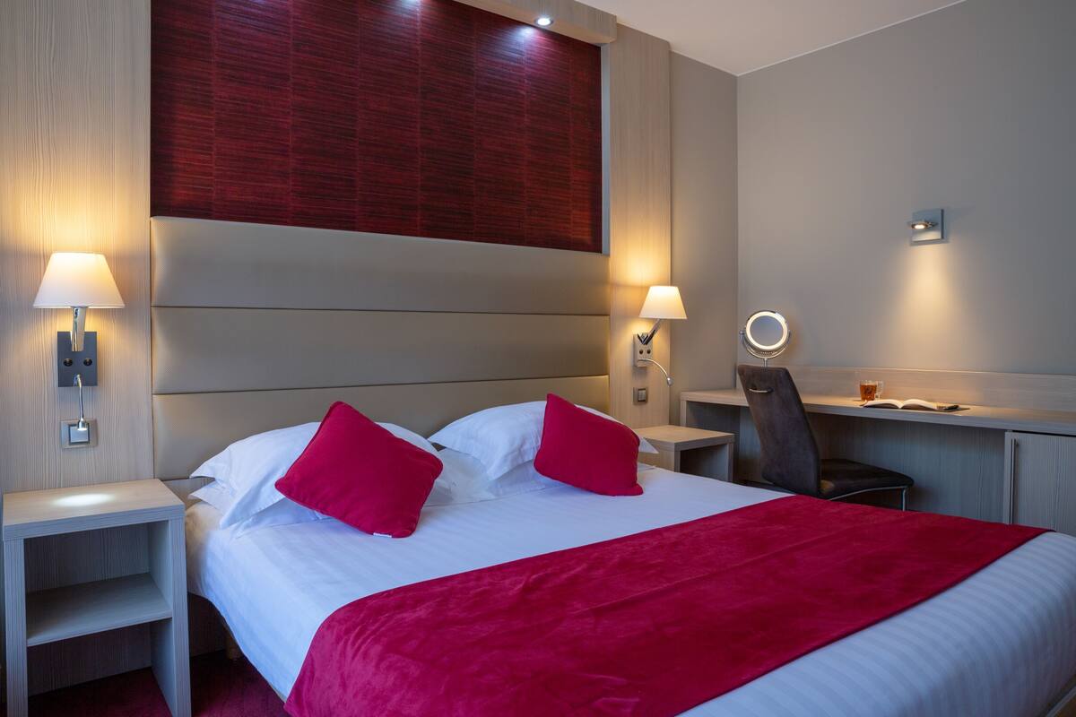 A hotel room with a bed, two bedside lamps, a desk with a chair, and a wall-mounted mirror.