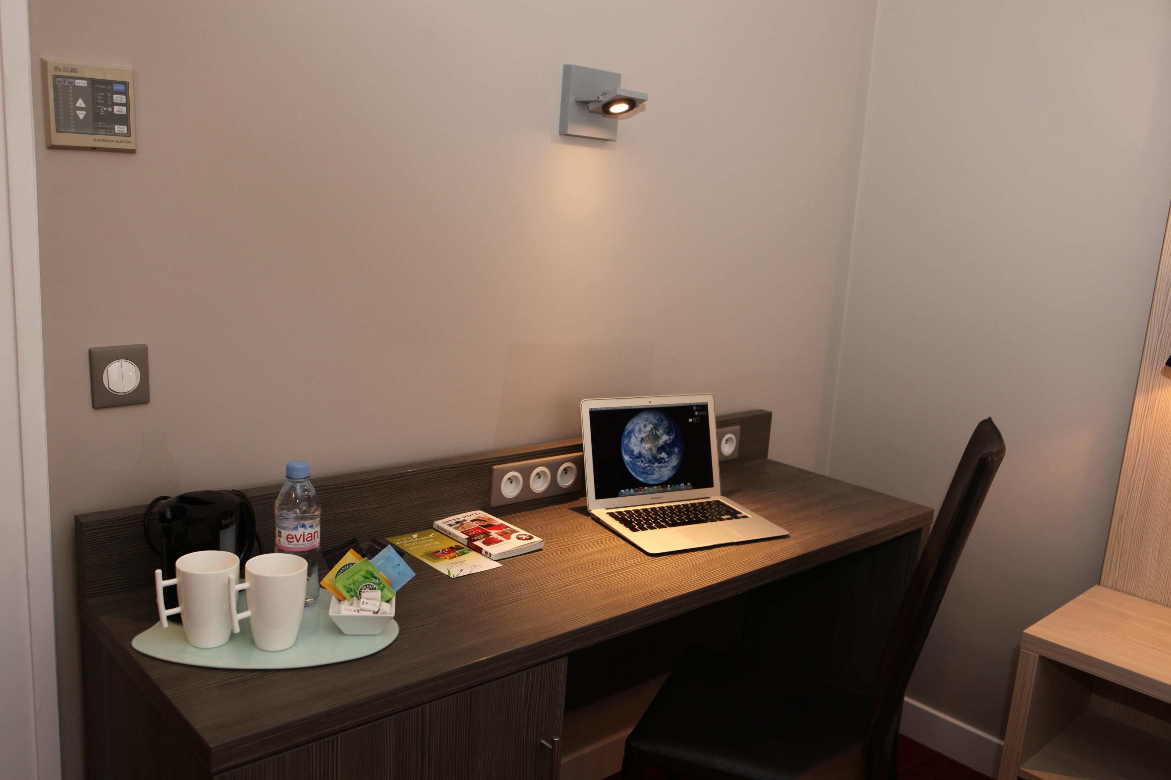 Habitació d'hotel amb un escriptori de fusta, un ordinador portàtil, una ampolla d'aigua i una cafetera.