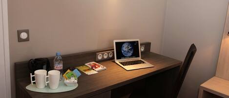 Habitació d'hotel amb un escriptori de fusta, un ordinador portàtil, una ampolla d'aigua i una cafetera.