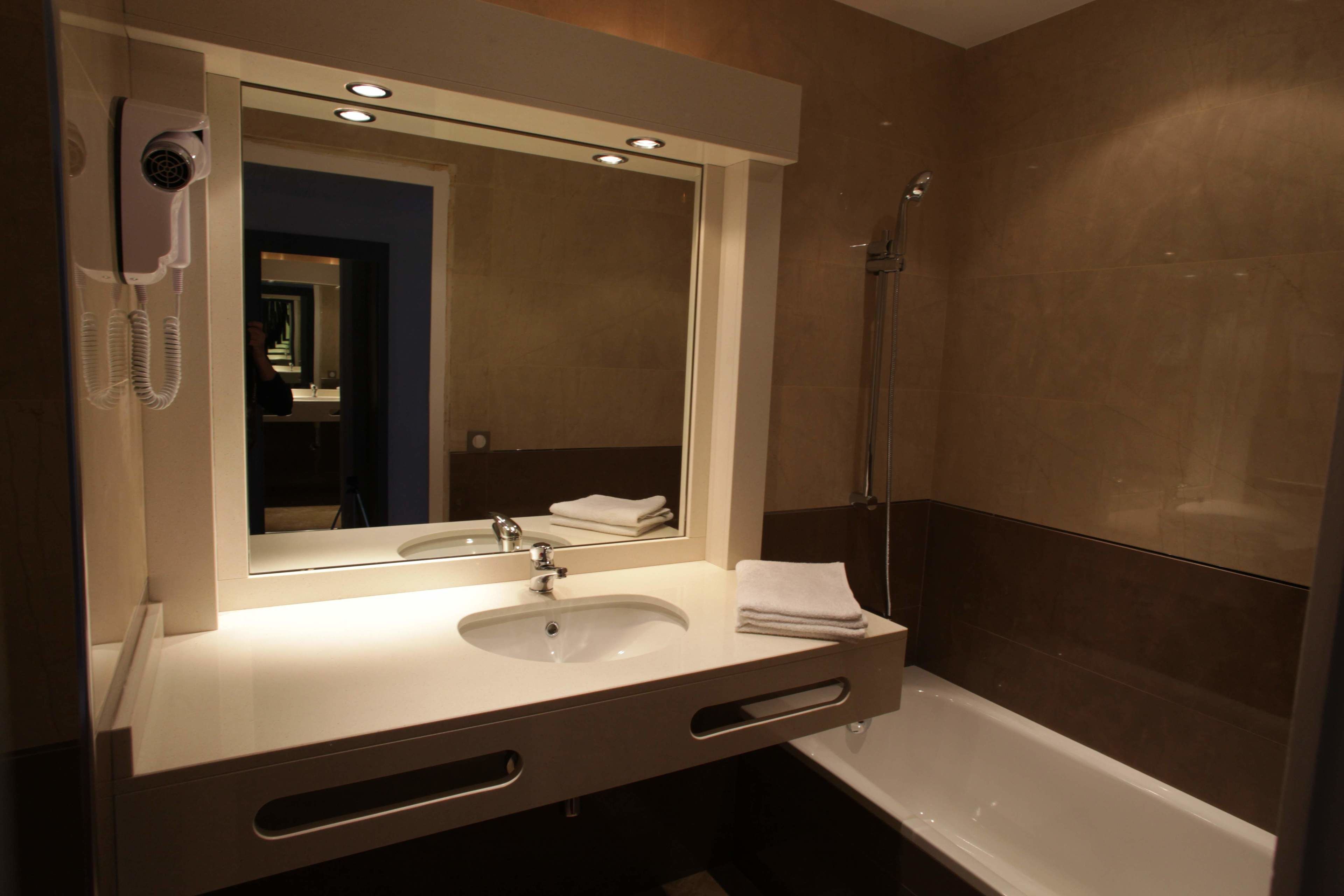 A modern bathroom with a large mirror, a sink, a hairdryer, and a shower.