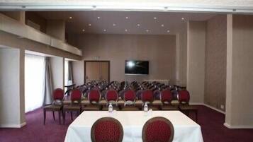 A conference room with rows of chairs, a long table, and a television screen on the wall.