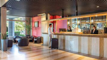 Una moderna hall d'albergo con reception, area lounge e ampie finestre.