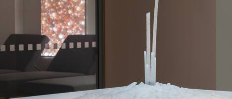 A modern interior with a minimalist ice sculpture centerpiece, a dark-toned sofa, and a window with a blurred view.