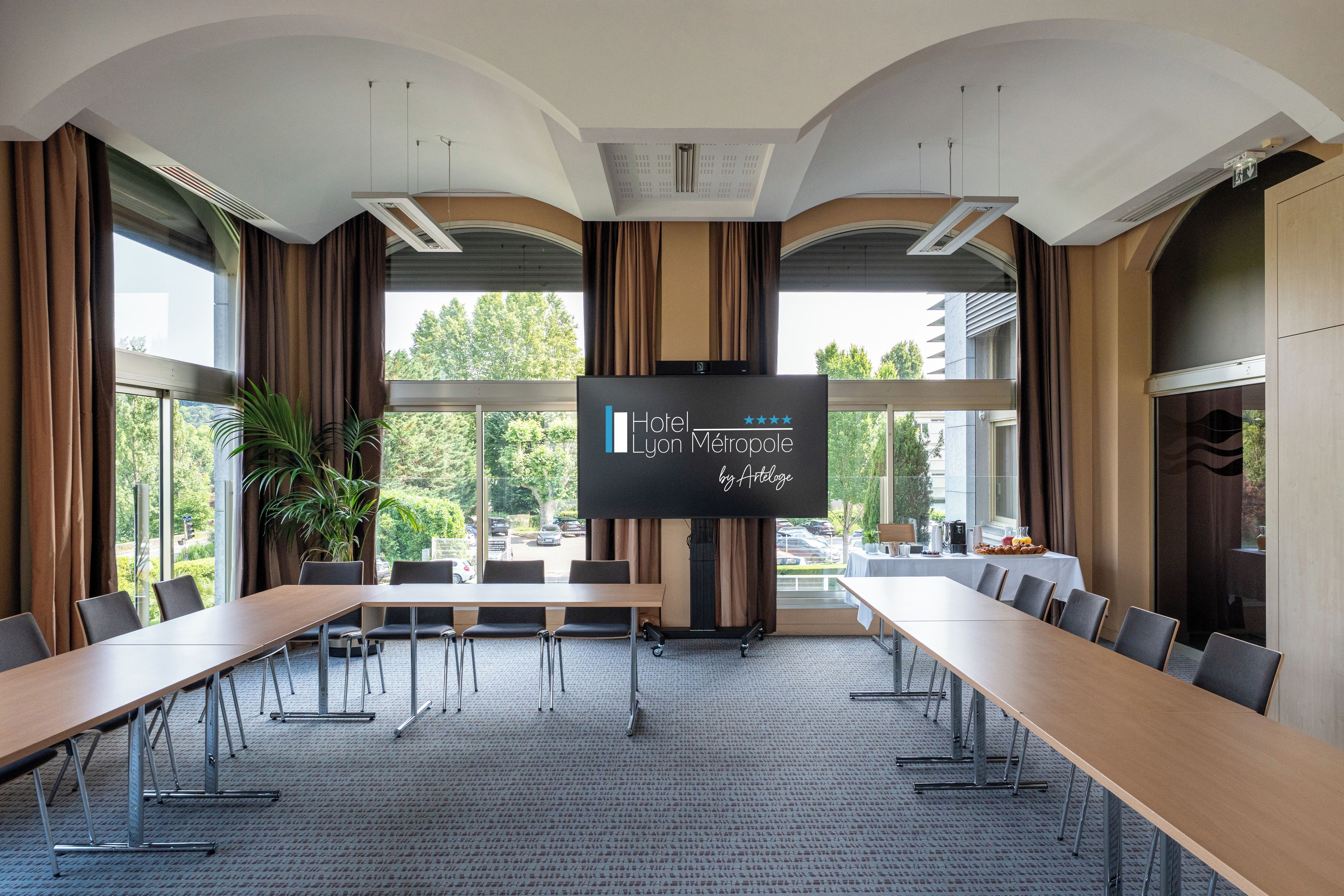 Un salón de conferencias con una gran mesa, sillas, una pantalla de proyección y amplias ventanas con cortinas.