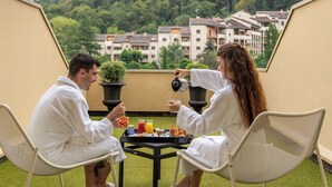 Two people in white robes sitting at a table with a tray of food and drinks on a balcony with a view of buildings and trees. - Hôtel Lyon Métropole & Spa (Lyon)