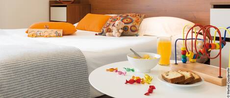 A hotel room with a bed, a bedside table with breakfast items, a wall with artwork, and a wooden headboard.