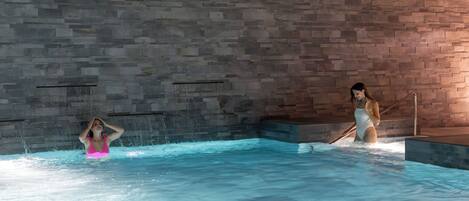 Une piscine intérieure avec des murs en pierre et un plafond en bois.
