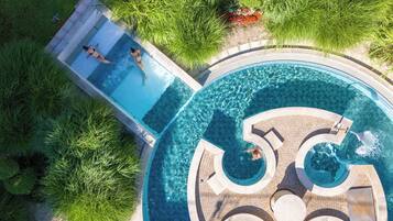 A large, multi-tiered swimming pool with clear water, surrounded by lush greenery and a tiled deck.
