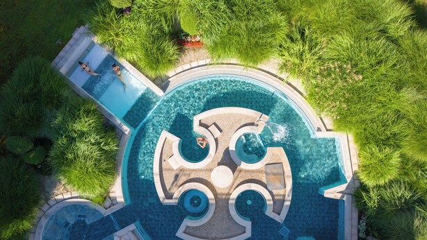 An aerial view of a circular swimming pool with a central fountain, surrounded by lush greenery. - Hôtel Lyon Métropole & Spa (Lyon)