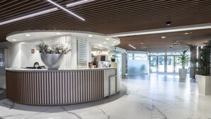 A modern reception area with a curved reception desk, a large vase of flowers, and a spacious lobby with marble flooring and large windows. - Hôtel Lyon Métropole & Spa (Lyon)