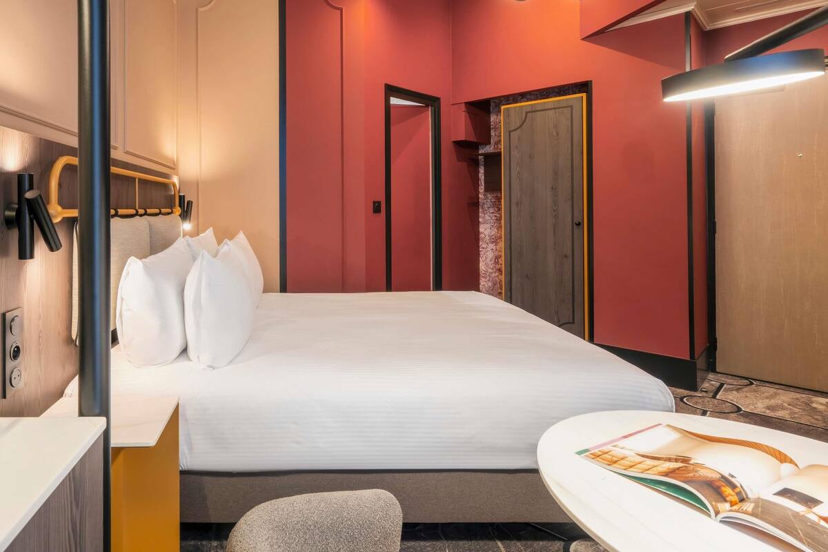 Una habitación de hotel con cama, mesita de noche y una revista sobre la mesa.