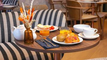 Ein Frühstückstisch mit Teekanne, Orangensaftglas, Croissants, einem Kiwi und einem Teller mit Speisen.