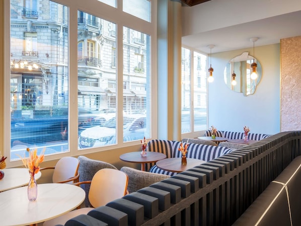 A modern interior with large windows, a curved bench seating area, and a round table with a vase. - Grand Hotel des Brotteaux Lyon Ctre - Handwritten Collection (Lyon)