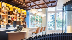 A modern interior with a curved seating area, a reception desk, and a decorative shelf with various items. - Grand Hotel des Brotteaux Lyon Ctre - Handwritten Collection (Lyon)