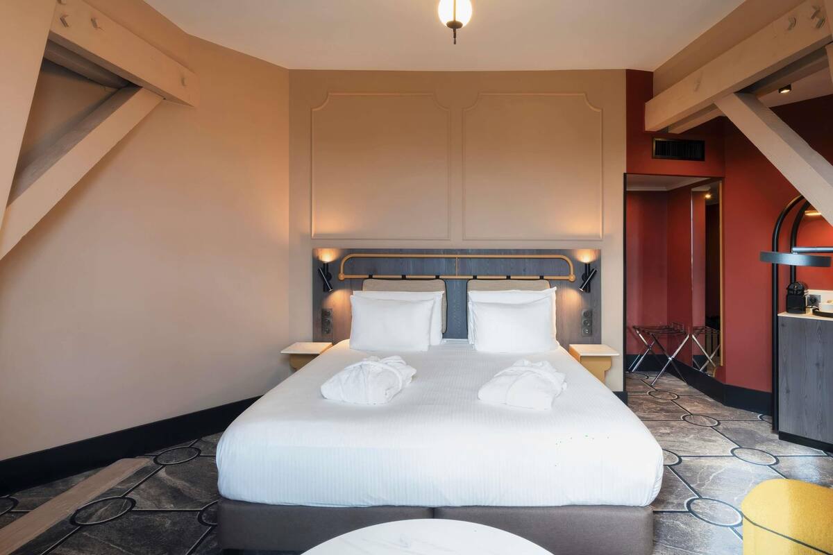 Una habitación de hotel con una cama grande, mesitas de noche, una lámpara moderna y una pared de acento roja.