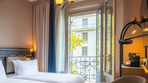 A hotel room with two beds, a small round table, a chair, a balcony with a view of buildings, and a coffee machine. - Grand Hotel des Brotteaux Lyon Ctre - Handwritten Collection (Lyon)