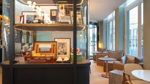 A modern interior with a glass display case, seating area, and large windows. - Grand Hotel des Brotteaux Lyon Ctre - Handwritten Collection (Lyon)
