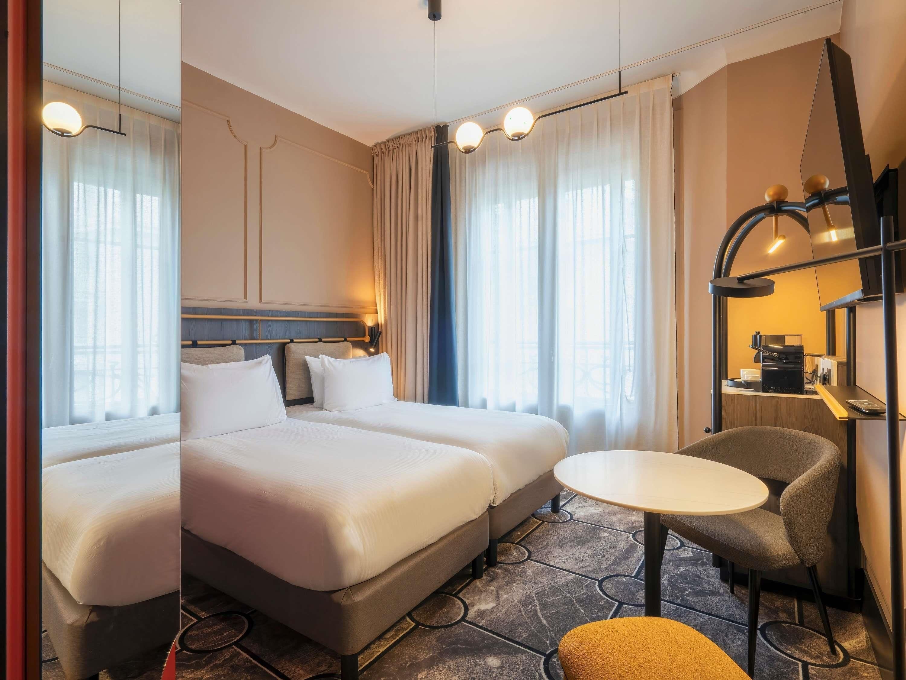 A hotel room with two beds, a small table, a chair, and a coffee machine.